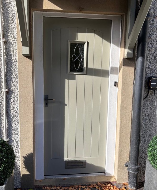 A grey front door with decorative glazing and silver furniture